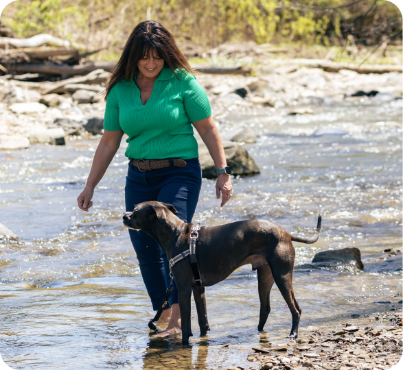 Dog trainer Lisa Yasenchak exploring a shallow creek with a black dog.